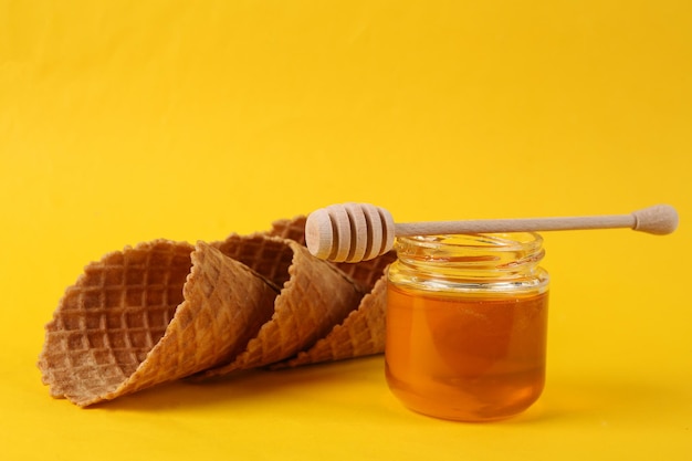 Jar of honey with waffle cones on yellow background
