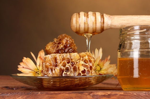 Jar of honeyhoneycombs and wooden drizzler on table on yellow background