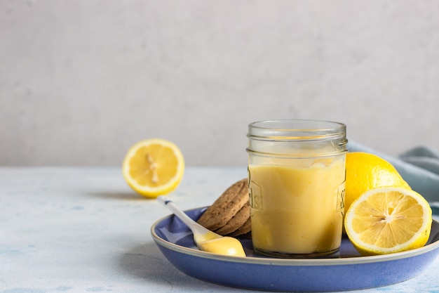 A jar of lemon curd or custard and cookies on a blue plate. 