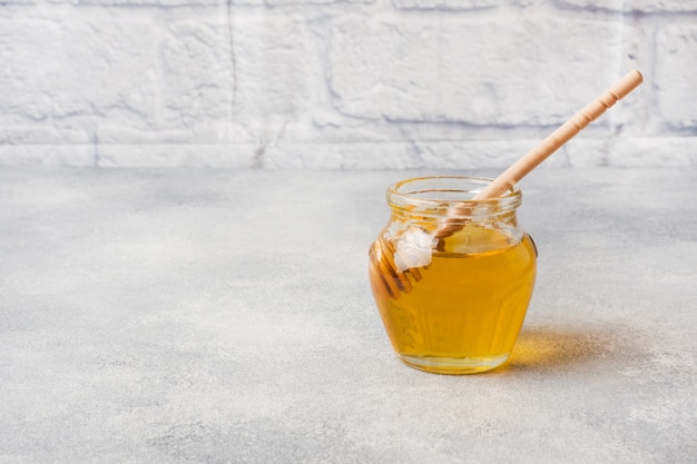 Jar of liquid honey and a stick on grey concrete surface. Copy space.