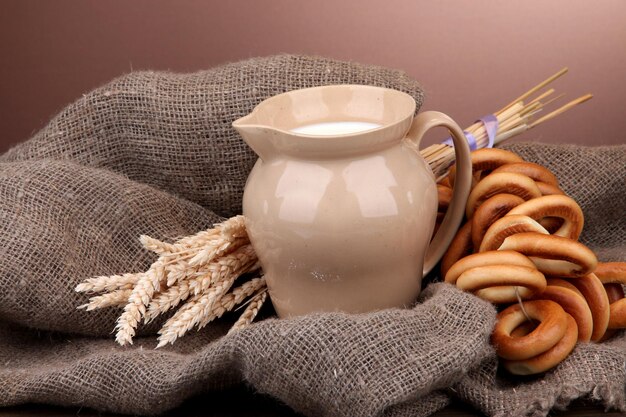 Jar of milk tasty bagels and spikelets on wooden table on brown background