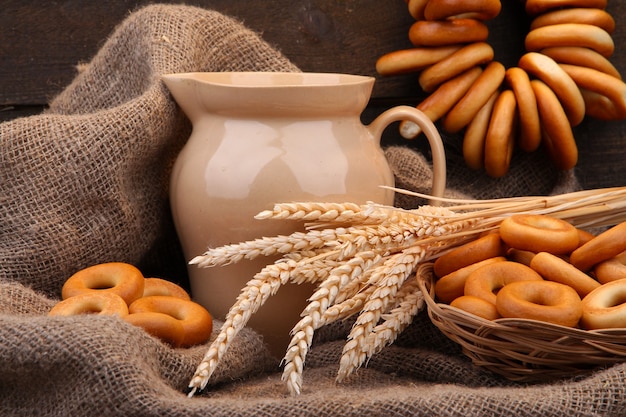 Jar of milk, tasty bagels and spikelets on wooden table