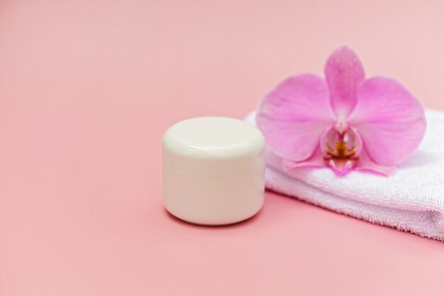 Jar of moisturizing body cream, bath towel, orchid flower on a pastel pink background. Skin care cosmetic concept. Soft selective focus. Copy space.