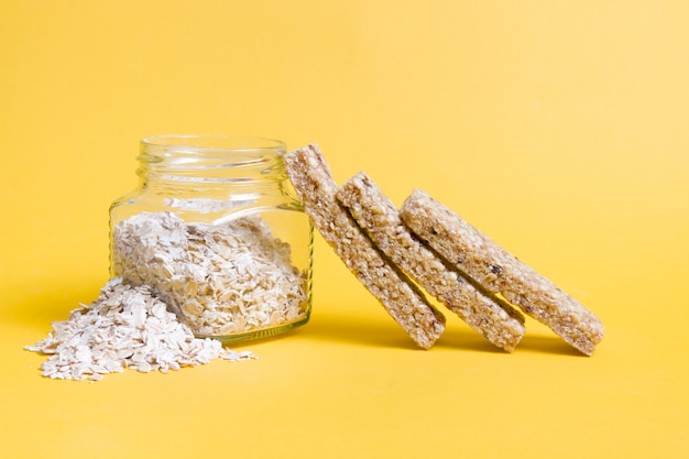 Jar of oatmeal and cereal bars on yellow background