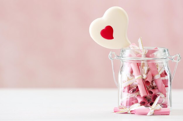 Jar of papers with sweet heart on table on bright background