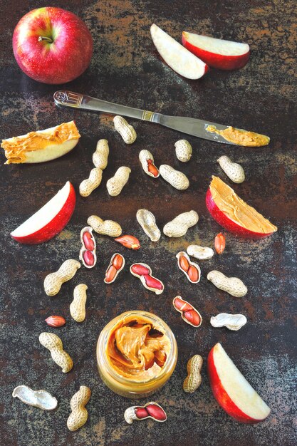 Jar of peanut butter, peanuts in a peel, apple slices and a knife