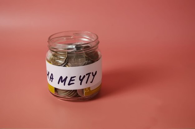 Jar piggy bank with an inscription on a dream with coins on a pink background