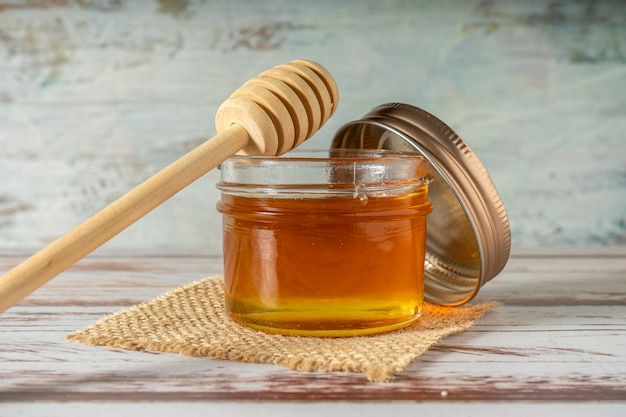 Jar of pure honey from bees with the wooden honey stick resting on the jar on an old rustic table.