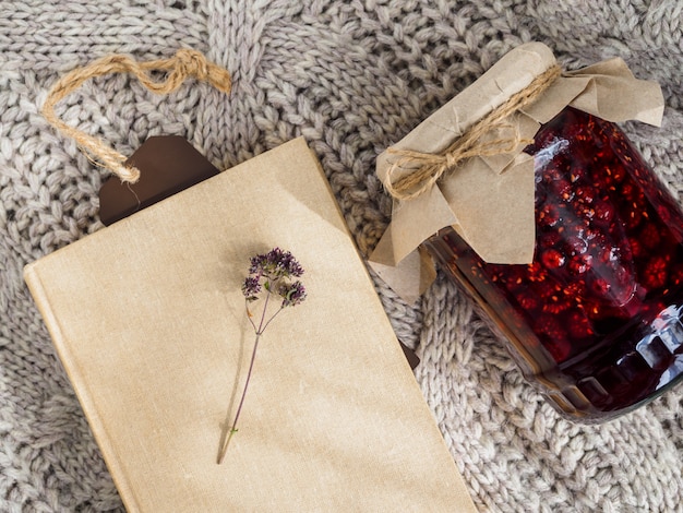 A jar of raspberry jam, a book and a sprig of scented on a wool blanket