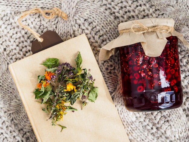 A jar of raspberry jam, dry herbs and a book lie on a woolen blanket.