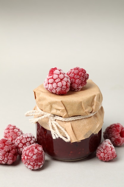 Jar of raspberry jam with ingredients on light background