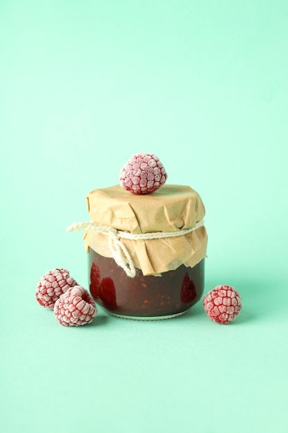 Jar of raspberry jam with ingredients on mint background