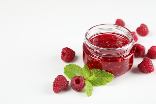 Jar of raspberry jam with ingredients on white background