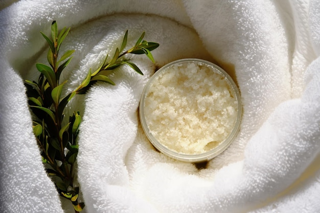 A jar of scrub wrapped in a terry bath towel with a green sprig