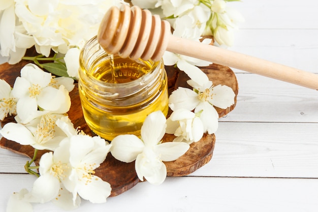 Jar and a spoon with honey on a wooden stand with Jasmine flowers