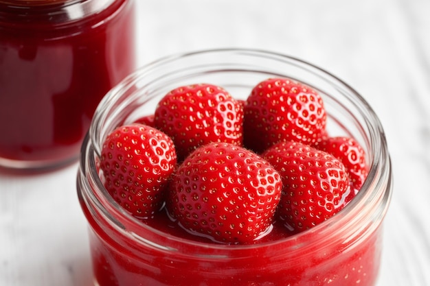 A jar of strawberry jam with a few strawberries on top.