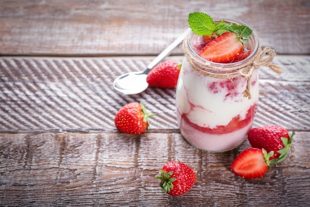 Jar of tasty strawberry dessert on wooden table