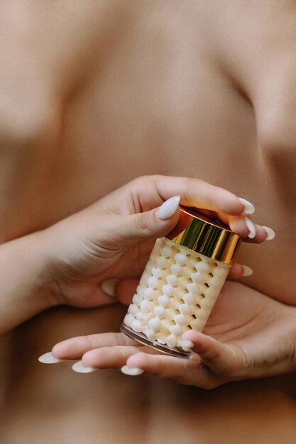 Jar of textured white cream in the hands of a beautiful girl on a background of bare back