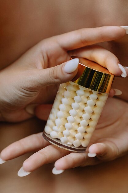 Jar of textured white cream in the hands of a beautiful girl on a background of bare back