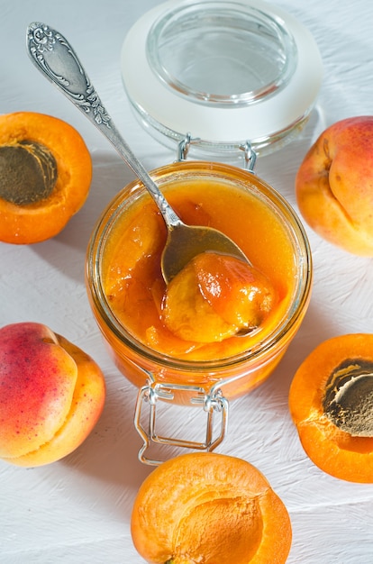 Jar with apricot jam and apricot fruit on a white wooden table. Top view, close-up.