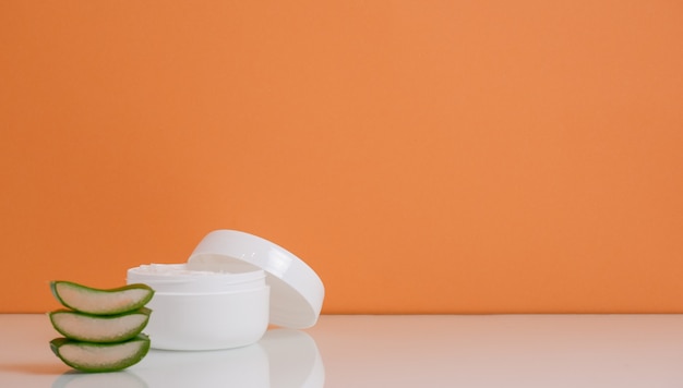 Jar with cosmetic cream and aloe vera leaves.