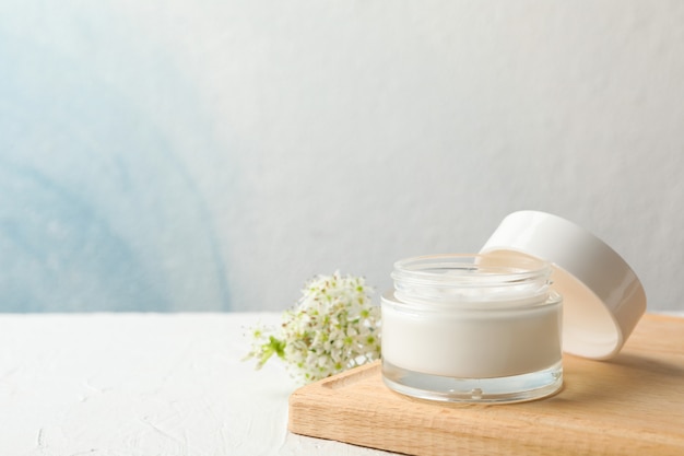 Jar with cream, allium flowers and board on white background