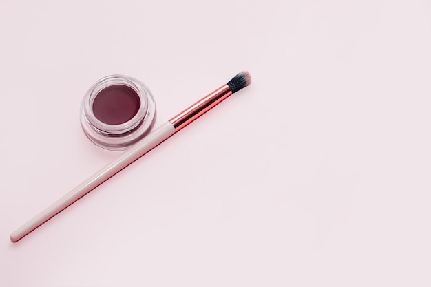 A jar with eyeshadow and eyebrow pomade on a white background