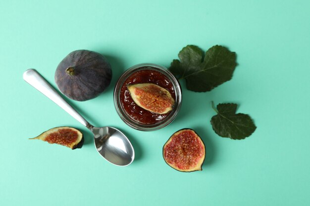 Jar with fig jam, ingredients and spoon on mint background