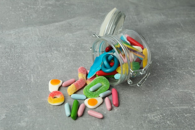 Jar with gummy candies on gray textured background.