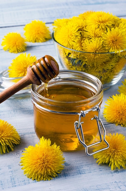 Jar with homemade honey of dandelion's flowers on light blue wooden table. close-up