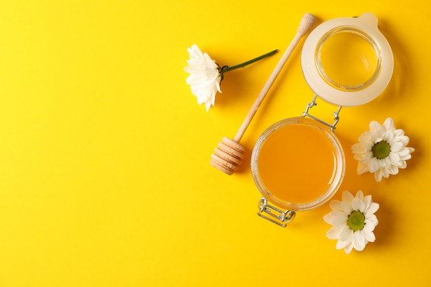 Jar with honey, dipper and chamomile on yellow background, space for text