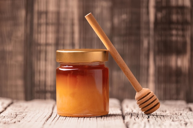 Jar with honey and dipper on a wooden background closeup