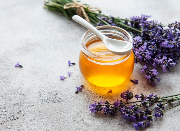 Jar with honey and fresh lavender flowers on a concrete background