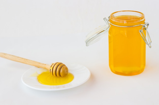 Jar with honey on a white table. Honey dipper on white