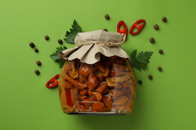 Jar with marinated mushrooms on green background