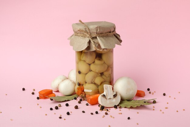 Jar with marinated mushrooms on pink background