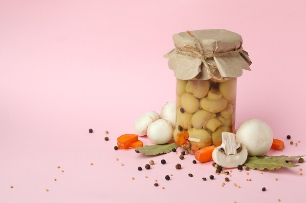 Jar with marinated mushrooms on pink background