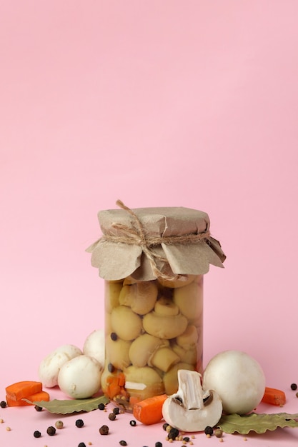 Jar with marinated mushrooms on pink background