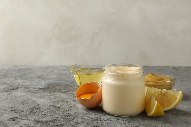 Jar with mayonnaise and ingredients for cooking on gray background