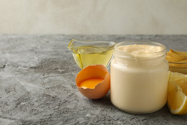 Jar with mayonnaise and ingredients for cooking on gray background