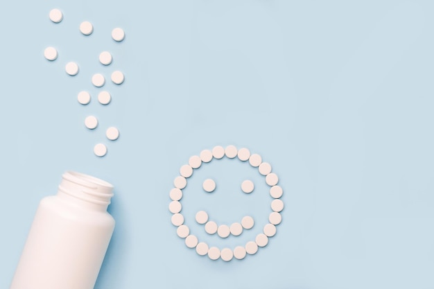 Баночка с лекарствами и счастливое лицо из таблеток на синем xAbackground Концепция антидепрессантов и исцеления
