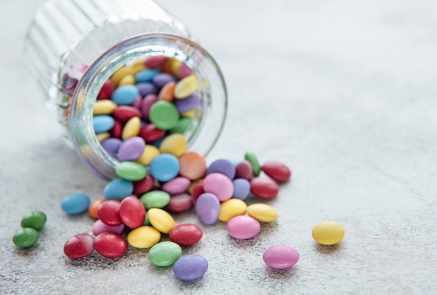 Jar with multicolored dragee sweets on a concrete desk