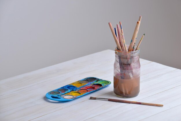 Jar with paintbrushes on work table with watercolors Copy space aside Ideal for art supplies creativity or painting concepts