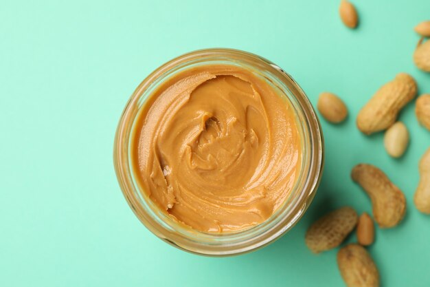 Jar with peanut butter and peanut on mint background