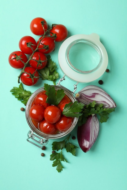 Jar with pickled tomatoes and ingredients on mint background