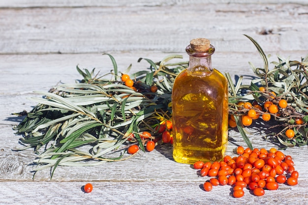 A jar with sea buckthorn oil and a fresh branch of sea buckthorn with berries on a wooden background