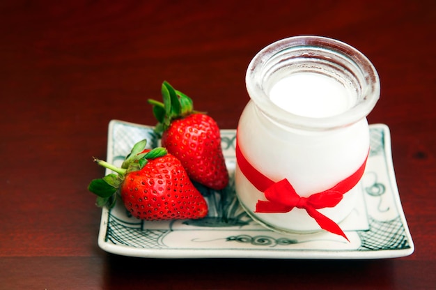 jar with yogurt and strawberries in plate on table
