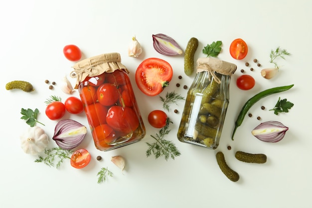 Jars of canned cucumbers and tomatoes, and ingredients on white