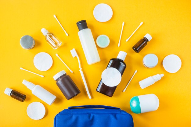 Jars and containers with cosmetics and cotton buds with disks from a blue cosmetic bag on a yellow background.
