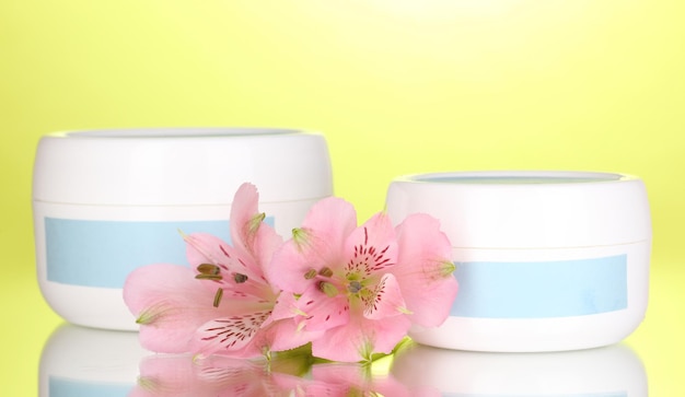 Jars of cream with flower on green background